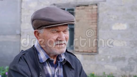 孤独的留着胡茬的老人正若有所思地悲伤地抽着烟在村里的大街上看着镜头穿着一件视频的预览图
