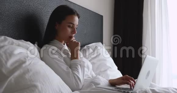 年轻女子躺在床上醒来后用电脑视频的预览图