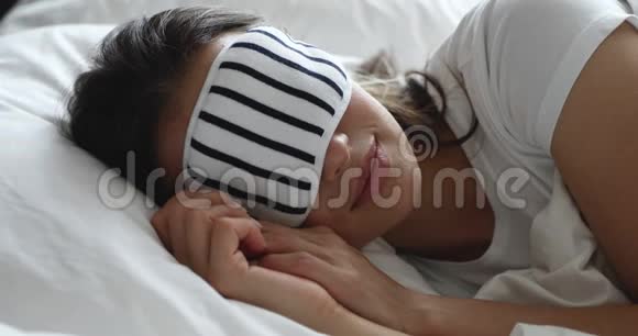 宁静的年轻女孩戴着夜间面具在舒适的床上放松视频的预览图