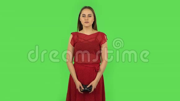 穿着红色连衣裙的小女孩正在用无线控制器玩电子游戏并为胜利而欢欣鼓舞绿色屏幕视频的预览图