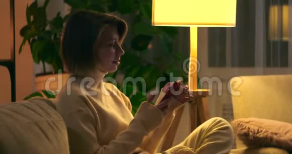 幸福的女人晚上在沙发上用手机视频的预览图