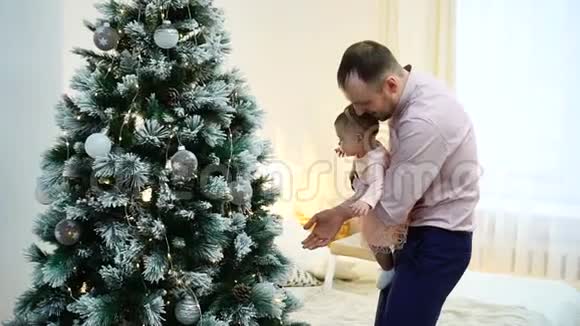 父亲抱着小女儿在家中靠近圣诞树家庭和父母身份视频的预览图