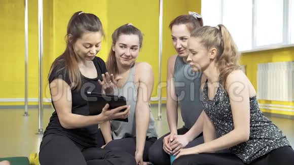 一群年轻的女教师在健身室的平板电脑上讲话并展示信息视频的预览图