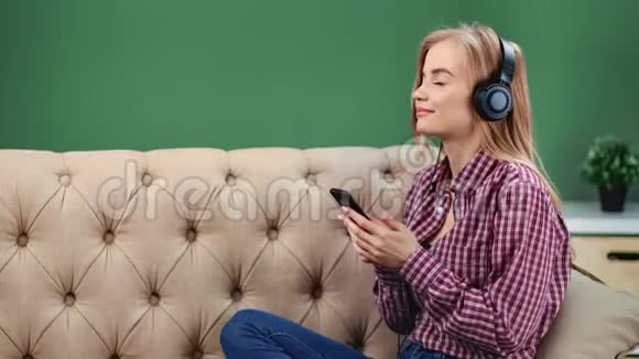 可爱的女孩戴着耳机听音乐用智能手机坐在沙发上4k龙红相机视频的预览图