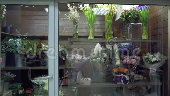 花店里的一个冰箱里一个年轻的女花匠在窗户上纠正花束和植物视频的预览图