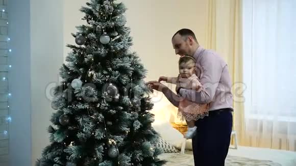 父亲抱着小女儿在家中靠近圣诞树家庭和父亲视频的预览图