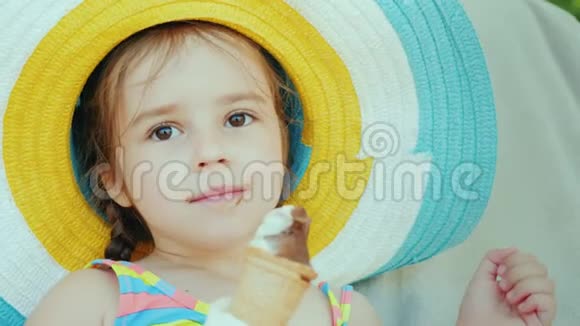 戴帽子的快乐女孩吃冰淇淋带着孩子在度假村放松视频的预览图