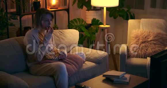 快乐的女人晚上吃爆米花看电视视频的预览图