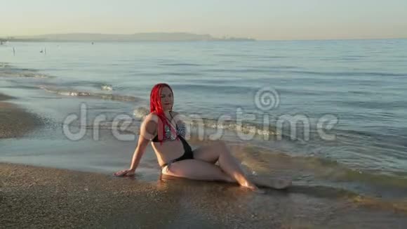 一个穿着泳衣的女人坐在海浪汹涌的海岸上视频的预览图