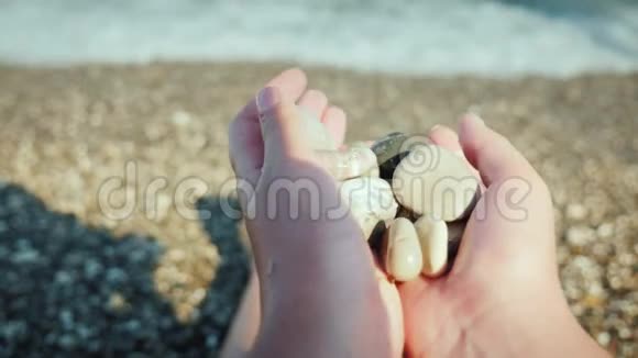 一个人拿着一把鹅卵石坐在海边的沙滩上视频的预览图