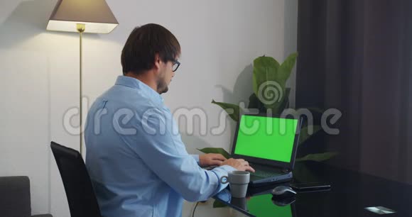 男人在家坐在沙发上用绿色的模拟屏幕笔记本电脑视频的预览图
