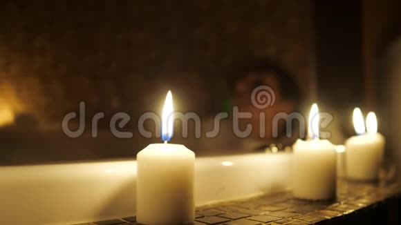 女孩躺在一个有泡沫的浴室里点燃蜡烛的特写视频的预览图