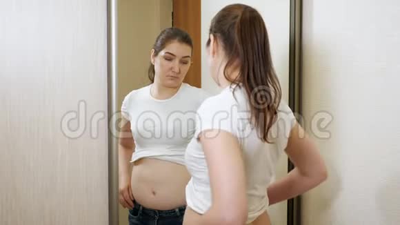 年轻的超重女性在镜子前触诊她的两侧和胃视频的预览图
