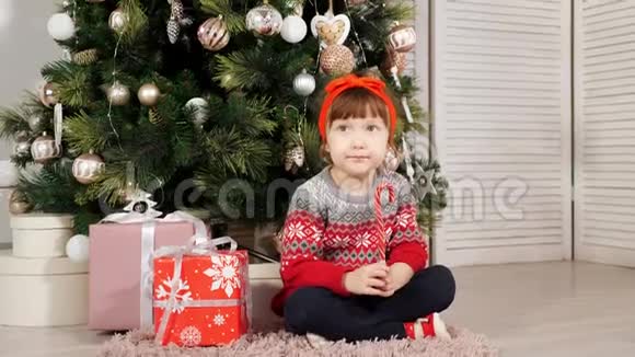 小女孩坐在圣诞树下笑着拍照视频的预览图
