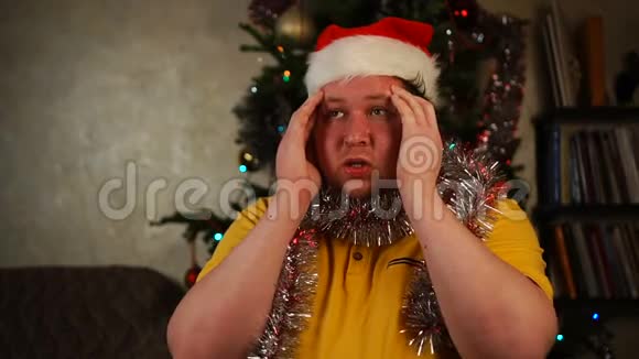 戴着圣诞帽和金箔的男人坐着头痛或紧张的情绪视频的预览图