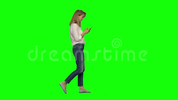 金发女人平静地走着在绿色屏幕上发短信给她的手机铬钥匙4k射击侧写视图视频的预览图