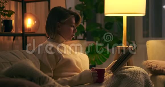 快乐的女人晚上喝咖啡和看书视频的预览图