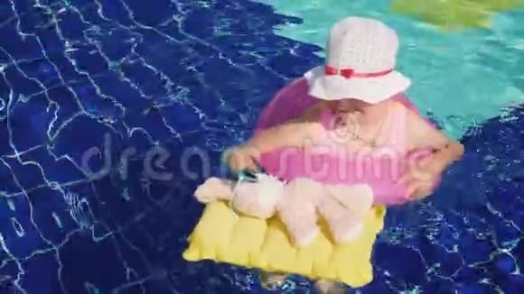 一个穿着泳装的有趣女孩和一个戴着墨镜的粉红兔子在游泳池里的充气圈里洗澡关节视频的预览图