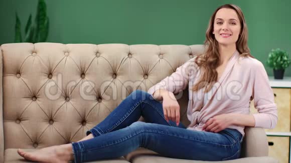 在舒适的家里一个轻松愉快的年轻女人在舒适的沙发上摆姿势4k龙红相机视频的预览图