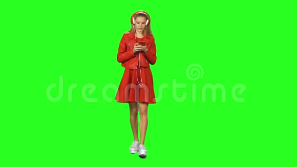 金发女孩戴着红色的大耳机行走选择音乐在绿色屏幕上移动节奏视频的预览图