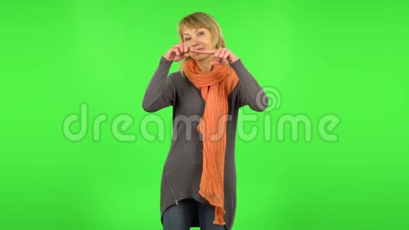中年金发女人微笑着用手指露出心脏然后吹吻绿色屏幕视频的预览图