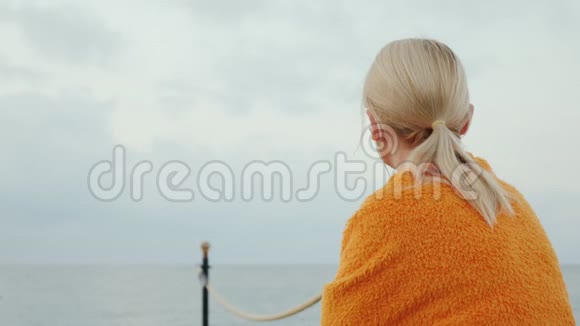 一个清凉的早晨梦幻般的女孩坐在码头上在毯子里翻找用耳机听音乐视频的预览图