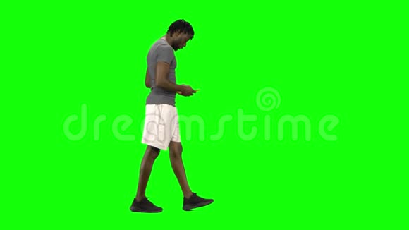 非裔美国人走路和发短信给他的手机在绿色屏幕Chroma键侧写视图视频的预览图