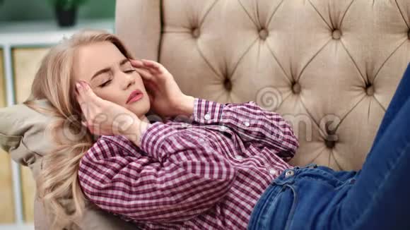 沮丧的休闲女孩摸着头感觉疼痛放松在舒适的沙发上4k龙红相机视频的预览图