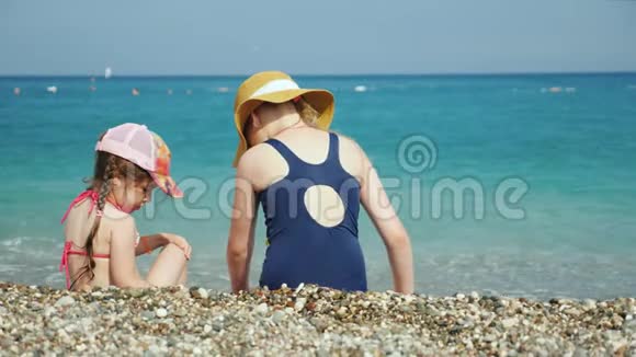 两个女孩坐在海边的小石子上寻找美丽的小石子海上儿童度假概念视频的预览图