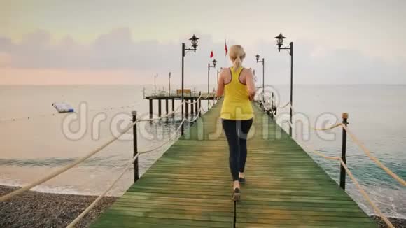 积极的生活方式一个穿运动服装的年轻女孩在码头上晨跑迎接日出视频的预览图