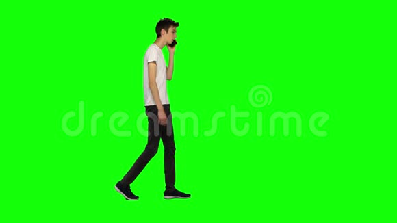 一个瘦高个儿的小伙子在绿色屏幕上平静地走着用手机聊天彩色键4k镜头纵断面图视频的预览图