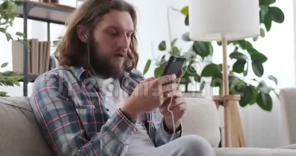 男人在家里用耳机和手机听音乐视频的预览图