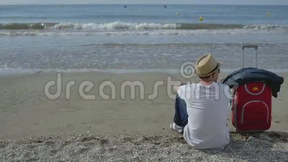 那家伙坐在海边来度假旁边有一个红色的手提箱视频的预览图