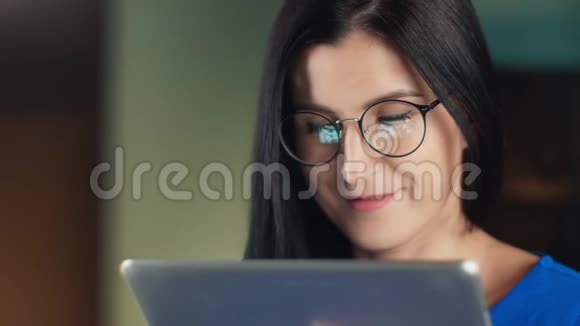 闭上微笑的黑发女孩戴着眼镜看着平板电脑上的照片4K红色相机拍摄视频的预览图