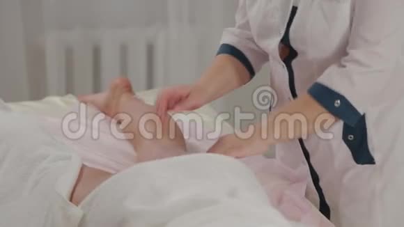 女性按摩治疗师在按摩室里按摩一个年轻女孩的腿视频的预览图