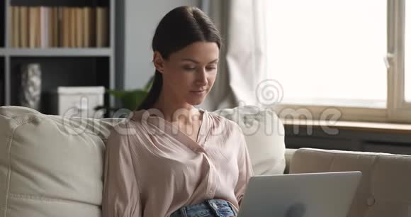 兴奋的女人坐在沙发上用笔记本电脑得到惊人的报价视频的预览图