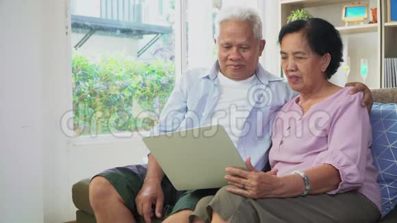一对幸福的亚洲夫妇坐在沙发上用笔记本电脑和家人一起上网和视频会议技术概念视频的预览图