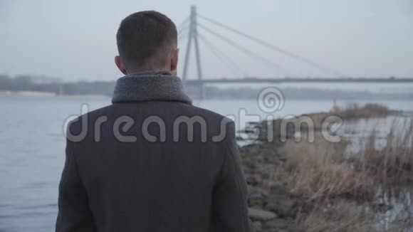后景优雅的白人男子站在河岸和看城市桥梁的背景孤独的黑发女人视频的预览图