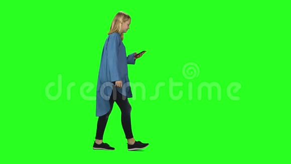 金发少女平静地走着在绿色屏幕上的手机上交谈铬钥匙4k射击侧写视图视频的预览图