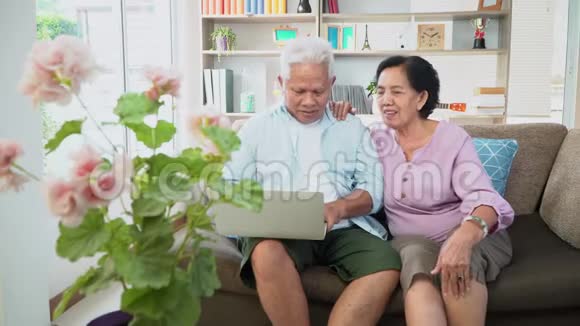 一对幸福的亚洲夫妇坐在沙发上用笔记本电脑和家人一起上网和视频会议技术概念视频的预览图