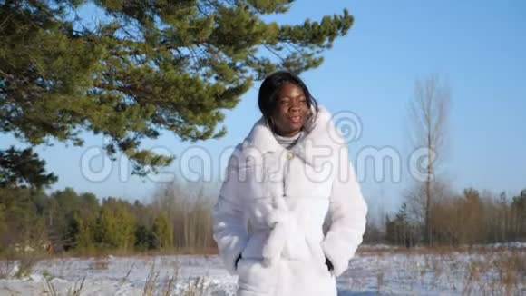 一个深色皮肤穿着皮衣的女人走在雪白的林间空地上视频的预览图