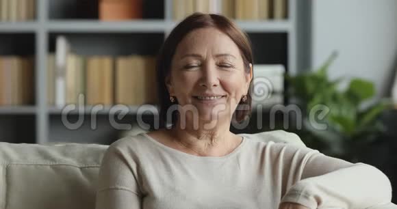 微笑着年长的女士在家里摆着相机视频的预览图