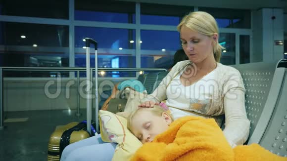 一个女人正在抚摸一个睡在她腿上的女孩坐在机场的终点站航班延误概念视频的预览图
