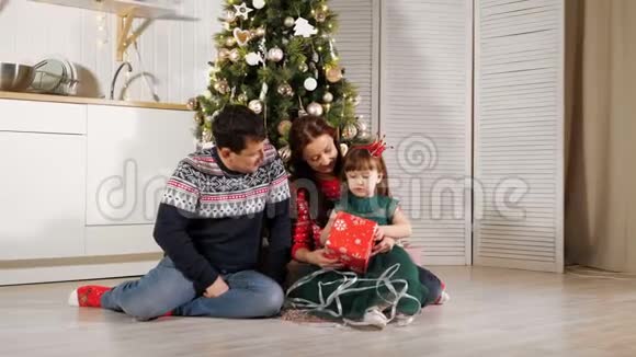 女孩与父母一起在圣诞树旁打开礼物盒视频的预览图