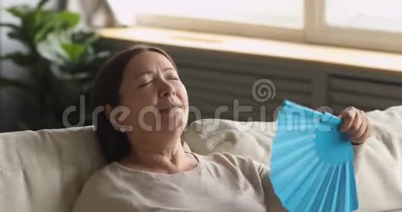 疲惫的老妇人挥舞着扇子感到不舒服在家热视频的预览图