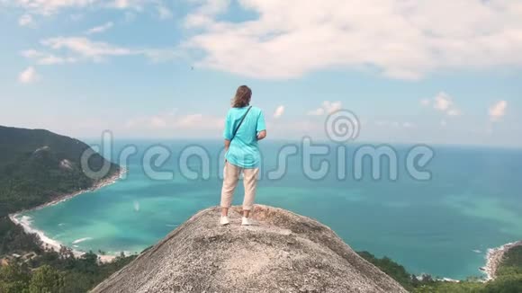 一个年轻的女人站在岩石的边缘有海景视频的预览图