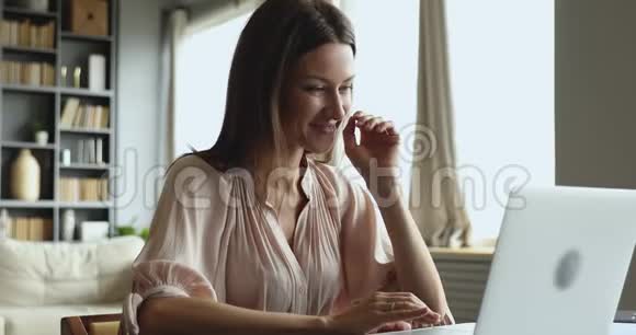 微笑迷人的年轻女子坐在桌旁用笔记本电脑打字视频的预览图