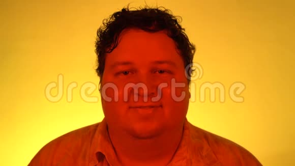 红色灯光下的人像拍摄一个胖子孤零零地站在黄色的背景上看着镜头微笑着视频的预览图