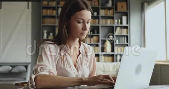 年轻的成年商务女性在笔记本电脑上打字坐在桌子上视频的预览图