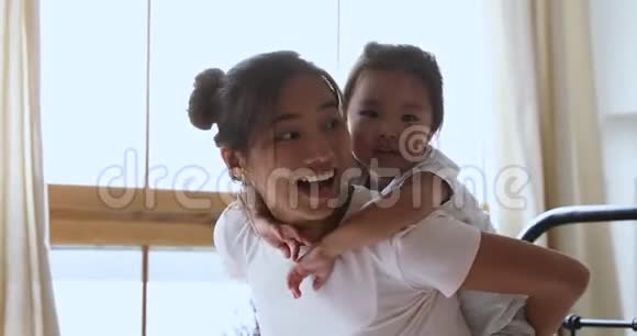 微笑亚洲妈妈驮着孩子女儿在床上嬉笑视频的预览图
